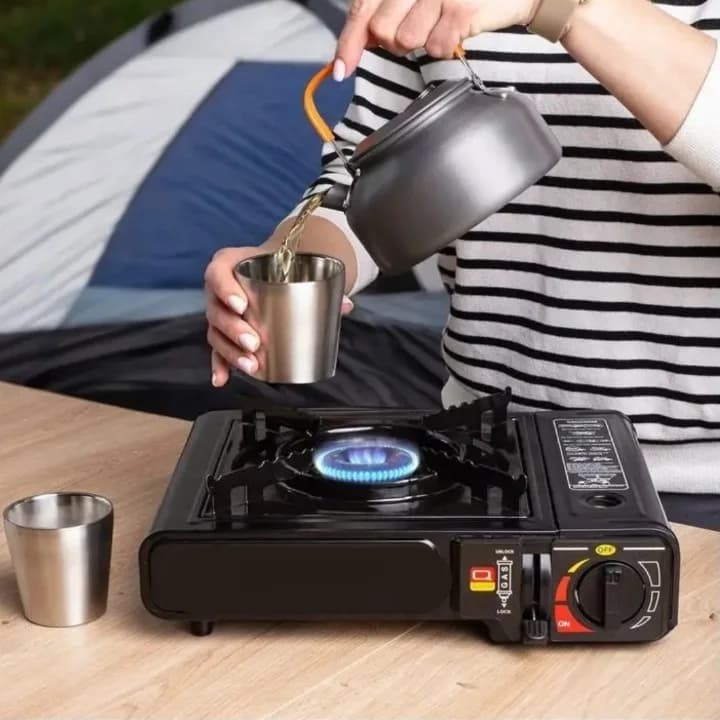 Stove in use in front of a tent, with a kettle pouring into a cup